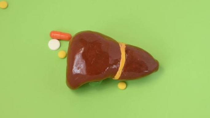 肝脏和药丸，药物，药物。肝脏疾病的治疗概念。药丸和胶囊从上方掉落在肝脏的解剖形状上，象征着药物对功能