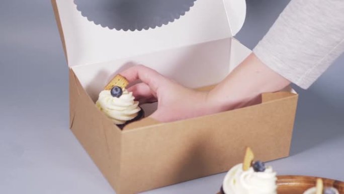 一个年轻女子的手将纸杯蛋糕装在一个带有丝带蝴蝶结的工艺盒中。