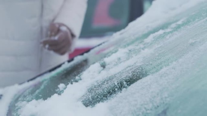 女性用彩色刷子清理车辆挡风玻璃上的湿雪