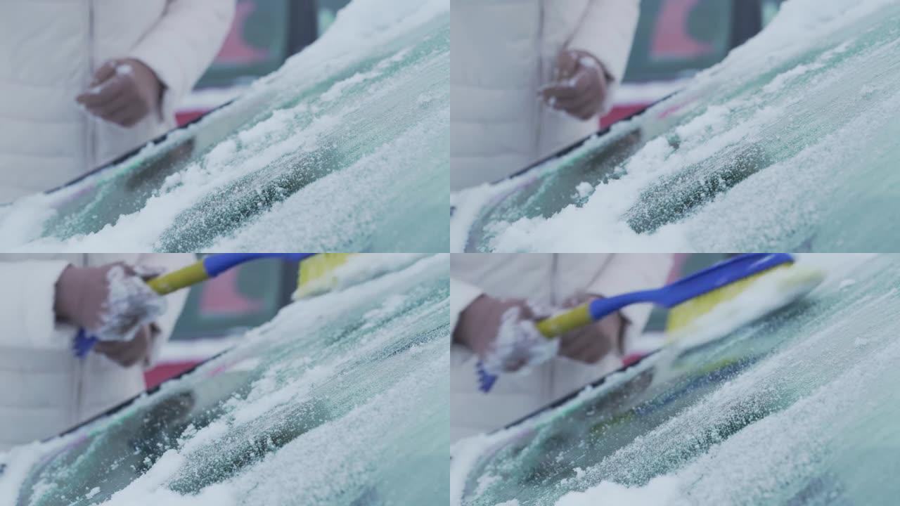 女性用彩色刷子清理车辆挡风玻璃上的湿雪