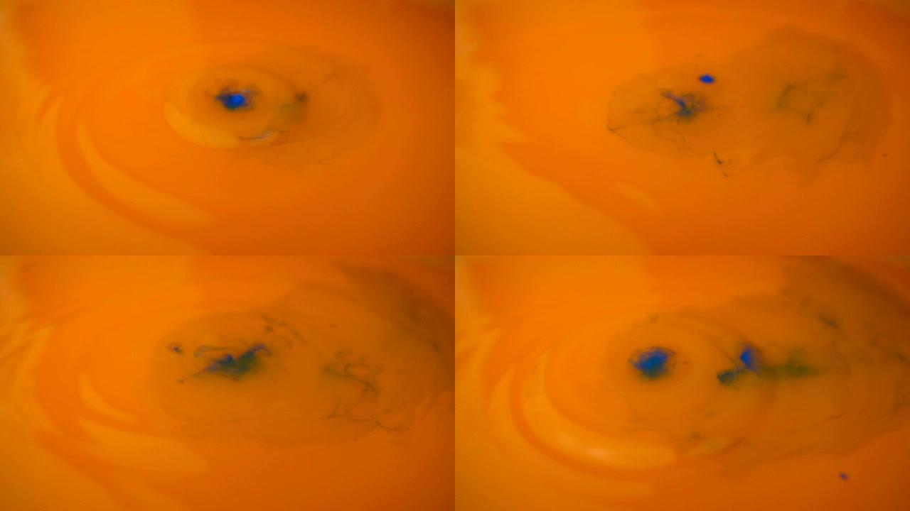 橙色油漆背景的微距摄影。蓝色油漆在慢动作中滴在橙色油漆上。