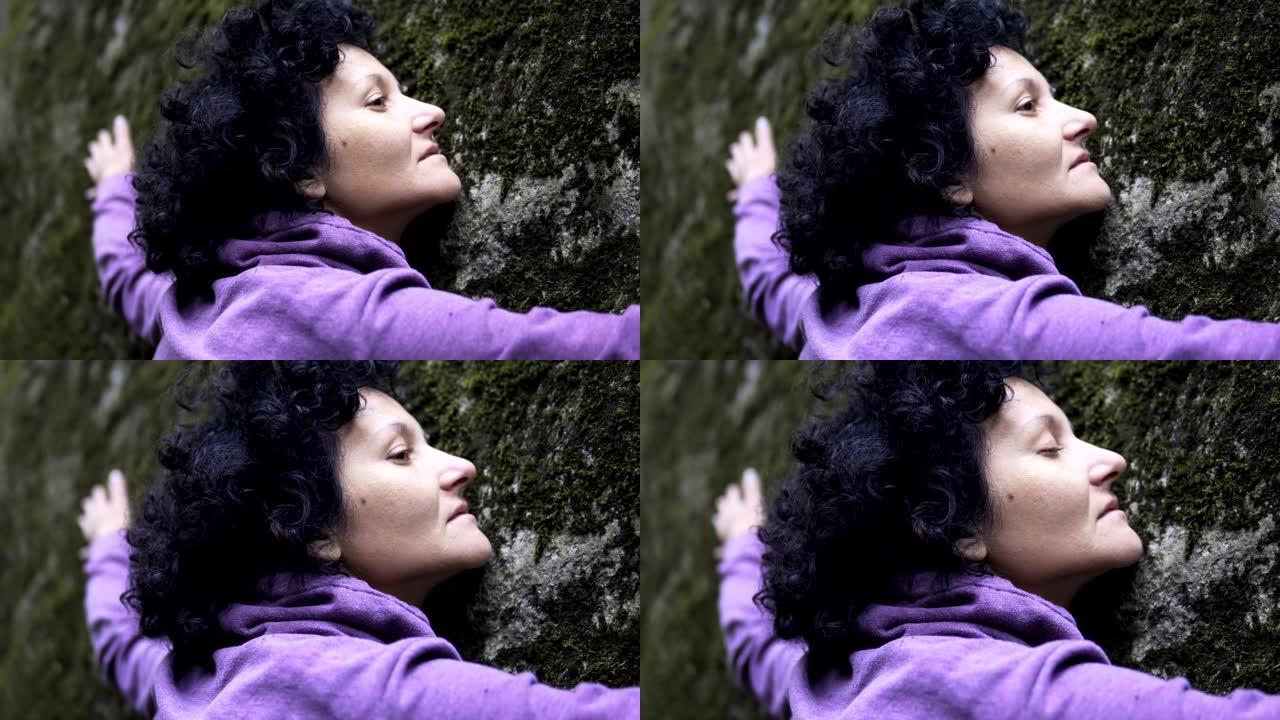 拥抱大自然。一个女人将手臂放在长满苔藓的大石头上，交换情感并从大自然中获取能量。