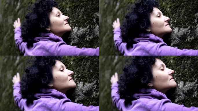 拥抱大自然。一个女人将手臂放在长满苔藓的大石头上，交换情感并从大自然中获取能量。
