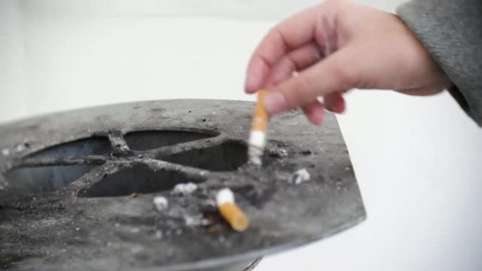 女孩的特写镜头在街道烟灰缸的边缘熄灭了一支香烟，并将其扔进了骨灰盒中。