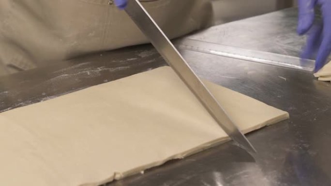 面包师手持刀并将viennoiserie面团切成三角形切片以制成羊角面包的特写镜头