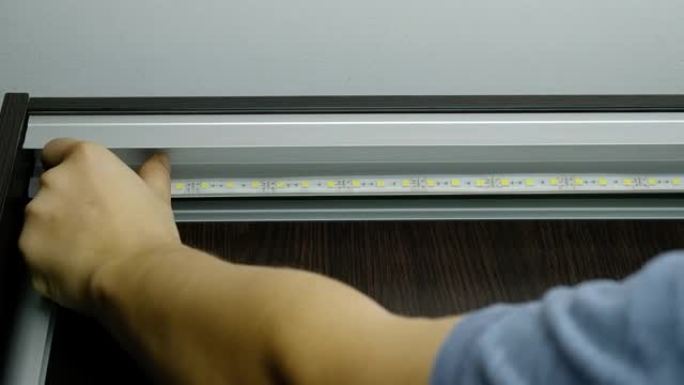 主人把发光二极管粘在橱柜上照明。二极管照明胶带的安装