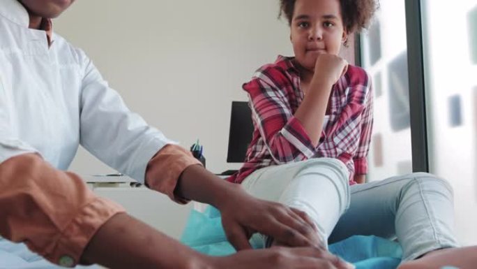 医生检查了一个非洲裔美国女孩的腿。腿部脱位急救。儿童入院时腿部骨折。儿童健康的概念。儿科医生，检查青
