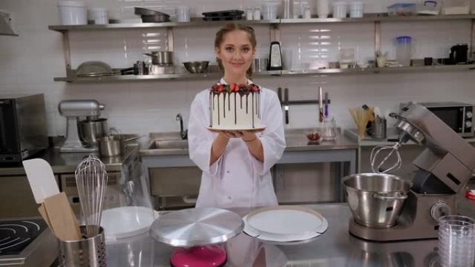一位女糕点师在专业厨房里拿着草莓蛋糕。