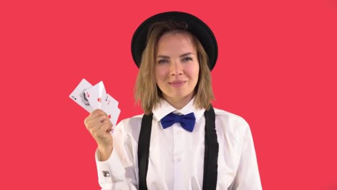 穿着白衬衫，帽子和领结的副主持人女孩表现出扑克牌和微笑。四张王牌，一个女孩眨眨眼。红色背景