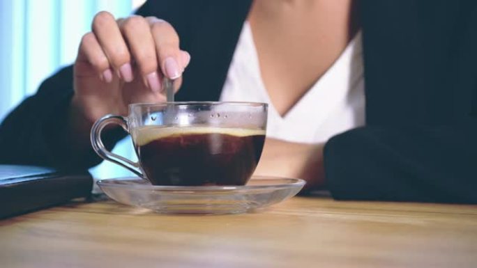 这个女孩穿着时髦的商务服装，坐在办公室里，把糖放在咖啡里。在此期间，它从中获得了极大的乐趣。