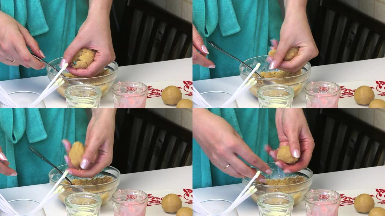 一个女人把饼干球卷成蛋糕。桌子旁边是装有糖霜，棍棒和盘子上准备好的球的玻璃杯。