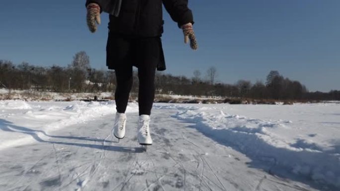 穿着裙子和白色花样溜冰鞋的浪漫年轻女子独自在冰冻的河上滑冰。冬季，女性的脚在冰上滑冰。户外滑冰
