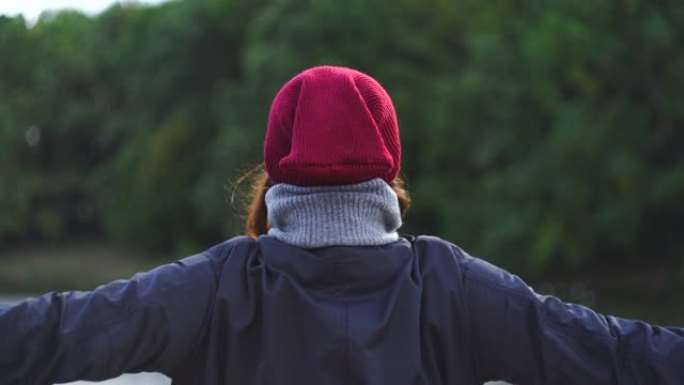 穿着暖和衣服的女人站在河岸上，欢欣鼓舞地张开双臂