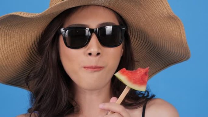 美丽的亚洲女人在蓝色背景下带着快乐的情感吃巧克力。美丽，时尚和夏季概念。