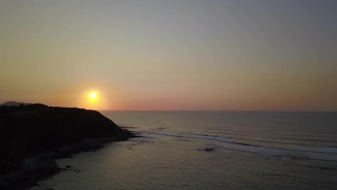 飞掠海滩的鸟瞰图，海浪逼近，日落时白色喷雾