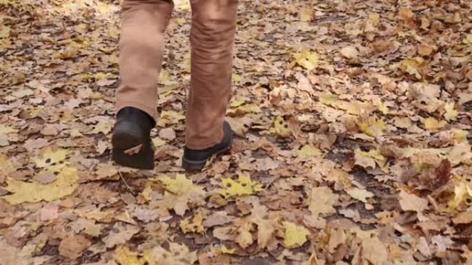 脚在地上行走慢动作视频。秋天的黄色叶子。在城市公园里穿着经典鞋子的男足