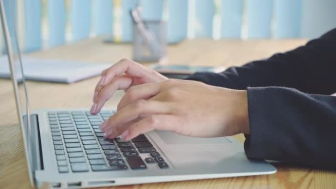 人的手在办公室背景的笔记本电脑上工作。办公室里的一名年轻女子在键盘上拨打文档。快速工作。