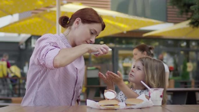 年轻的母亲和小女孩在咖啡馆吃冰淇淋。妈妈在女孩们的手上喷防腐剂。