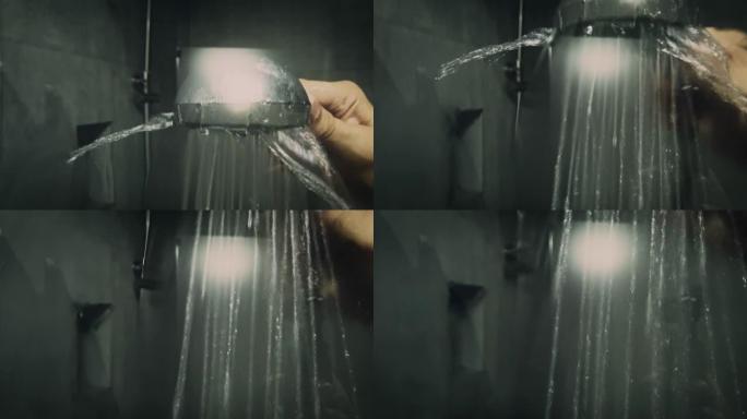 男子手持淋浴头在淋浴房玻璃后面的弱光拍摄