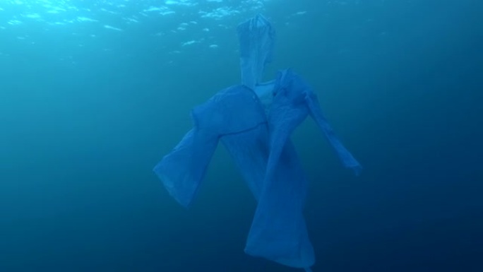 蓝色塑料雨衣作为幽灵在蓝色的水中慢慢漂浮。海洋的水下塑料污染。塑料垃圾环境污染问题。慢动作