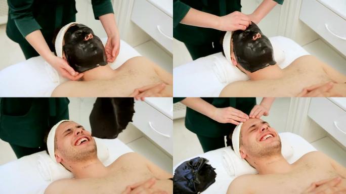 美容院的美容师从客户的脸上取下面膜。男士面部患者在美容水疗中心使用黑色面膜