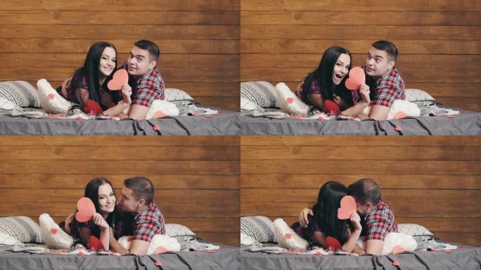 年轻夫妇躺在床上，心有红纸，看着相机。