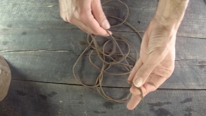 皮绳花边用手缠绕。自制。木质背景皮革制作，配有男士双手。4k，30 fps。