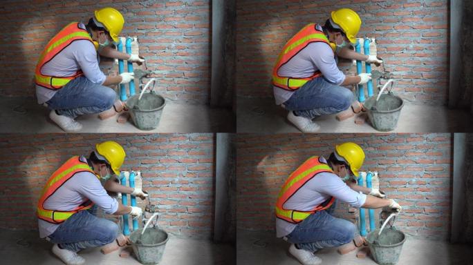 亚洲瓦工工人安装砖砌体封闭聚氯乙烯管，用于居住在新楼的水管系统
