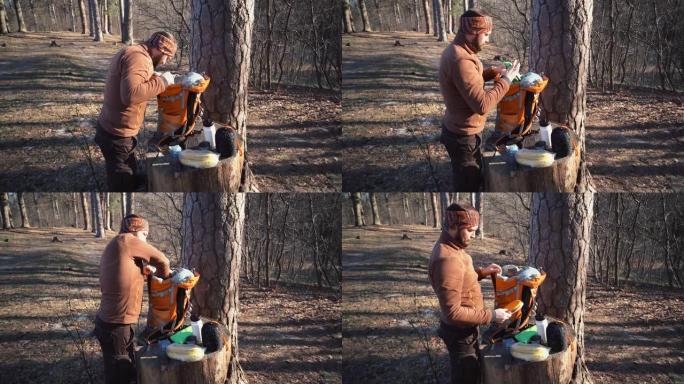 主题徒步旅行。一名高加索旅游男子打开一个橙色背包，拿出他的东西，放在森林的树桩上。露营的设备和东西。