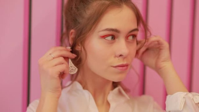 女孩在粉红色的墙上试戴耳环