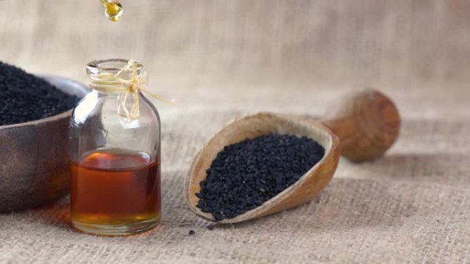 黑色孜然籽精油玻璃瓶，黑色木质背景上的黑种草，滴油