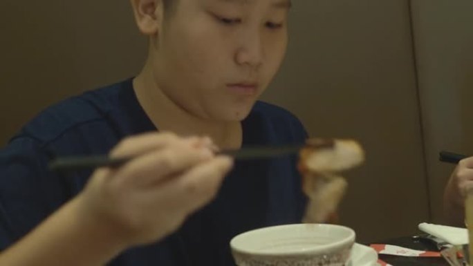 亚洲男孩在家庭，生活方式概念的餐厅里吃寿喜烧，sha锅或火锅。