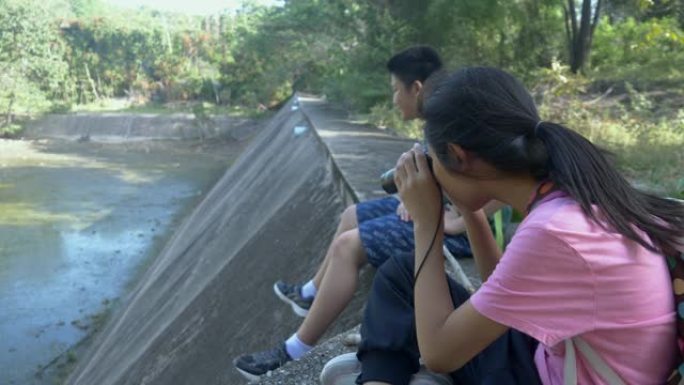 快乐的亚洲背包客儿童在大自然中放松，并使用双筒望远镜寻找动物，生活方式的概念。