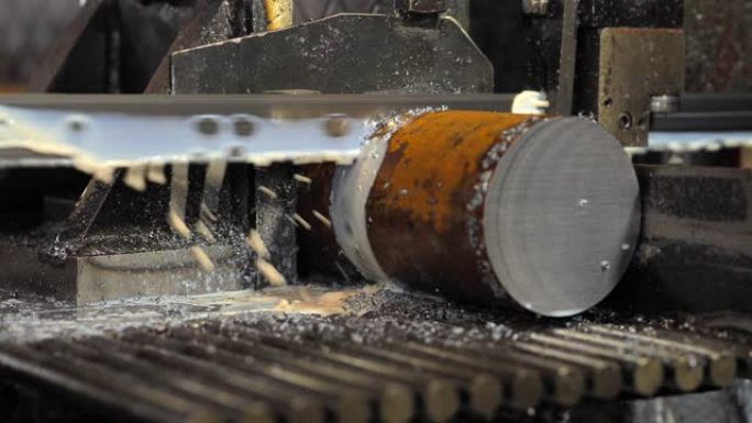用冷却液切割钢棒的工业机器。用冷却剂切割原始金属的带锯。