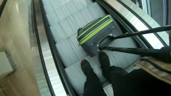 成年男子在机场自动扶梯上拖着行李箱