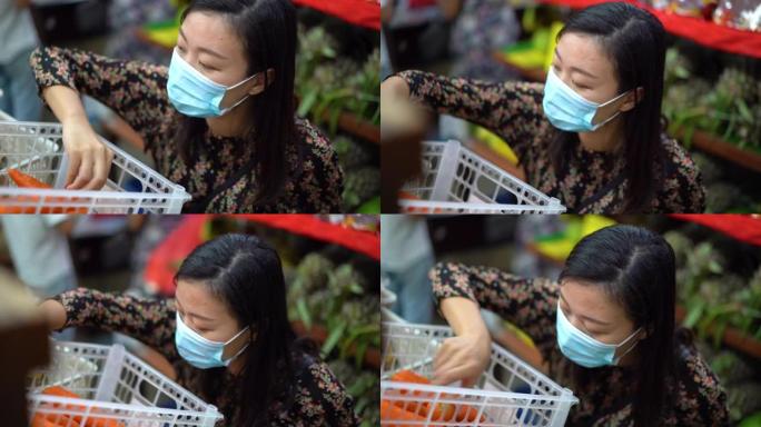 年轻的亚洲妇女戴着保护面罩在超市选购胡萝卜