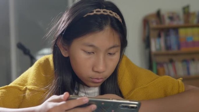 穿着黄色毛衣的亚洲女孩在家坐在椅子上观看病毒视频，生活方式概念。