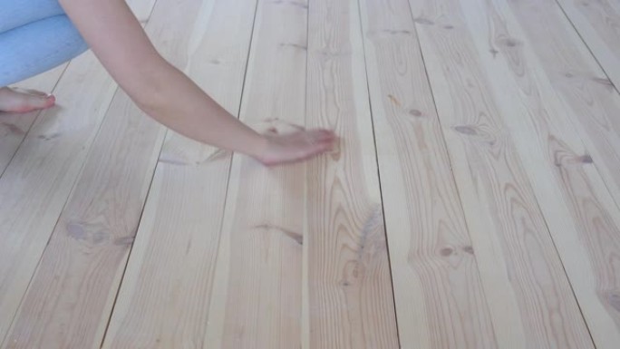 环保地板-赤脚的女人抚摸温暖的木地板特写。