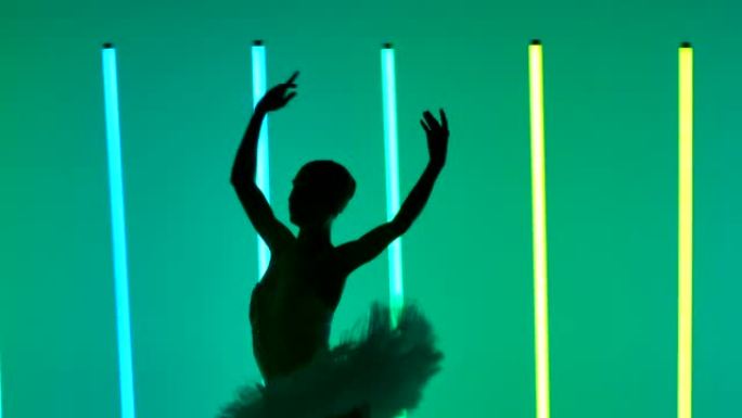 古典芭蕾编舞。年轻的芭蕾舞演员在明亮的霓虹灯的背景下，在黑暗的工作室中表演舞步。特写轮廓。慢动作