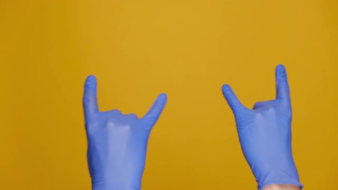 摇滚和大流行概念。用医用防护蓝色手套用喇叭手势挥舞着男性双手，隔离在黄色工作室背景上，有广告复制空间