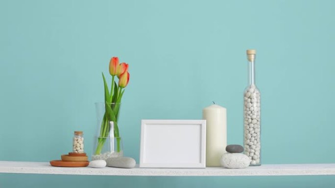 带相框模型的现代房间装饰。用装饰蜡烛、玻璃和岩石靠着绿松石墙。用手把郁金香放在花瓶里。