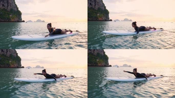 亚洲女子漂浮在sup板上，划桨板在夏日日落时穿过大海
