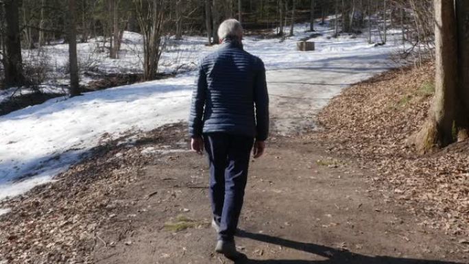 老人在阳光明媚的日子在春天的公园里散步