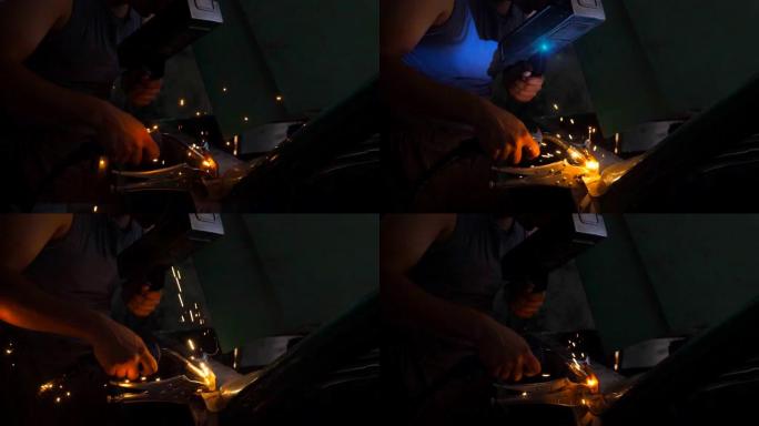 专业修理工或机械师的男工在车间使用焊接机焊接旧车的金属零件。车库黑暗中焊接工作产生的闪光和火花。侧视