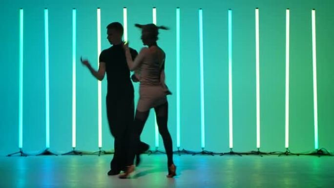 热情的年轻女子和她的伴侣在明亮的彩色霓虹灯上跳舞伦巴。一对美丽的舞者在慢动作中运动的剪影