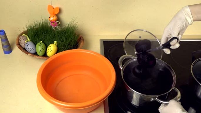 双手将彩绘的鸡蛋从带漆的锅中拿到带水的塑料碗中