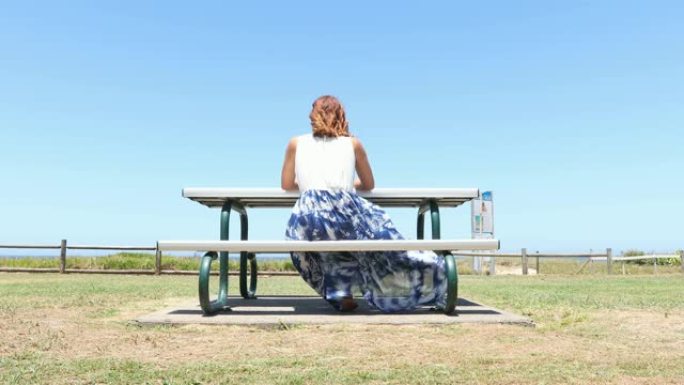 年轻女子坐在海滩旁的野餐座位上思考