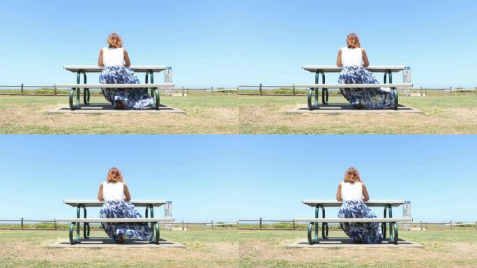 年轻女子坐在海滩旁的野餐座位上思考