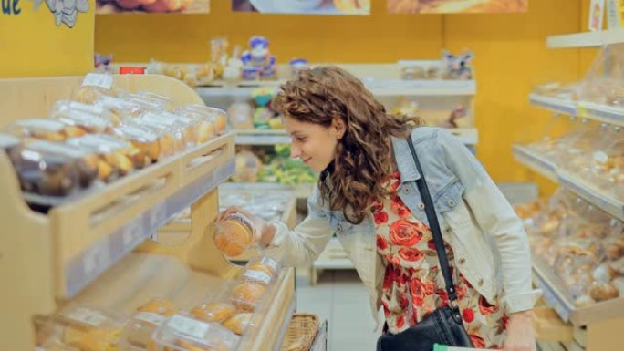 年轻漂亮的女孩在面包店的橱窗上选择面粉产品。美女从超市货架上拿甜甜圈。