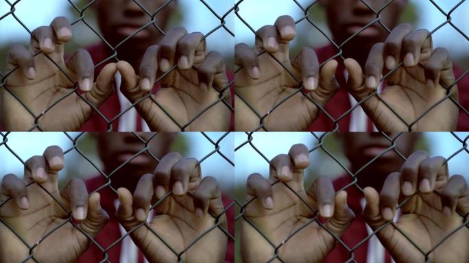 悲伤的年轻黑人非洲移民在监狱网后面。非法移民